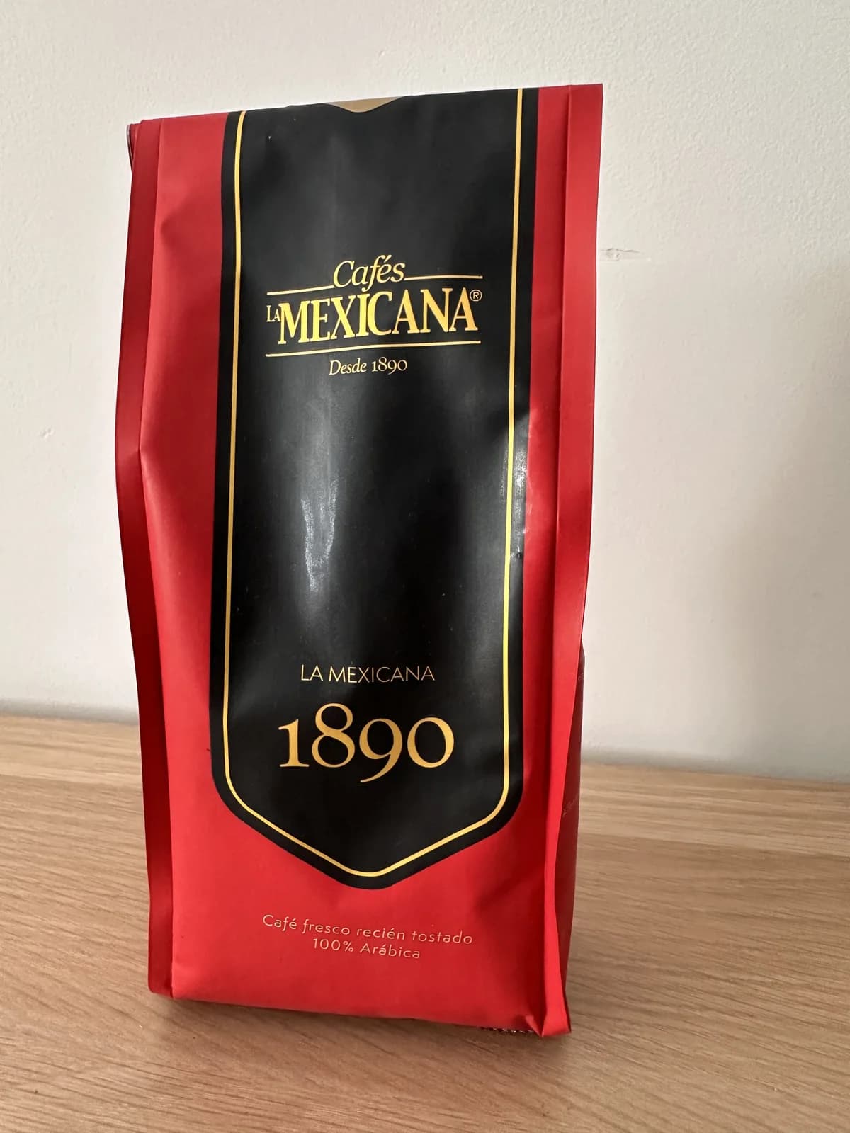 Bolsa roja y negra de café La Mexicana 1890, 100 % arábica, sobre una mesa de madera